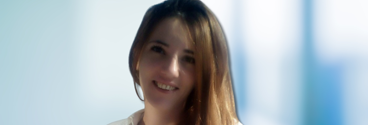 Žena duge smeđe kose nasmijana gleda u kameru, u svijetlom okruženju.