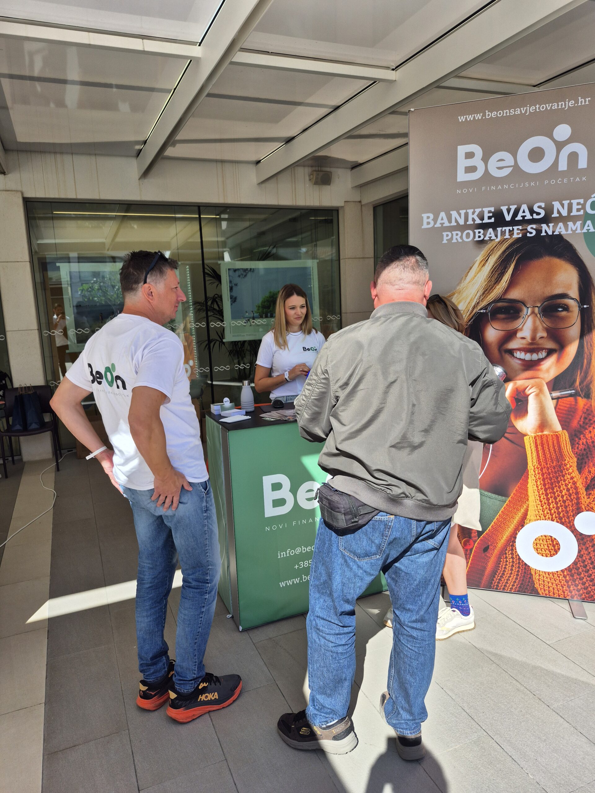 BeOn promotivni štand na otvorenom, s dvoje predstavnika u bijelim BeOn majicama koji razgovaraju s posjetiteljima.