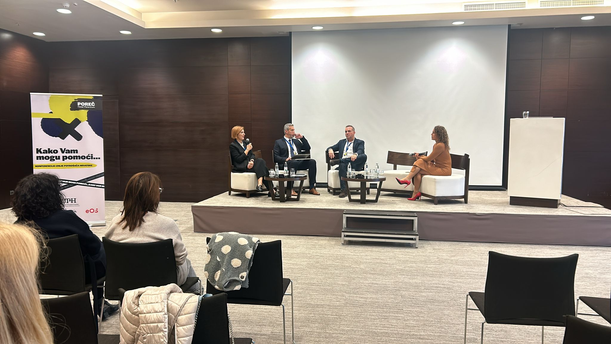 Panel rasprava na konferenciji u Poreču. Na pozornici sjede četiri osobe – tri muškarca i jedna žena – uključeni u razgovor, dok publika sjedi i sluša.