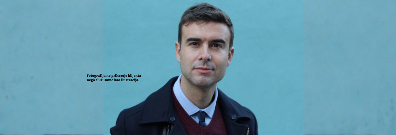 Muškarac srednjih godina u tamnom kaputu i košulji s kravatom stoji ispred plavo-zelene pozadine i gleda u kameru; fotografija je ilustrativna i ne prikazuje stvarnog klijenta.