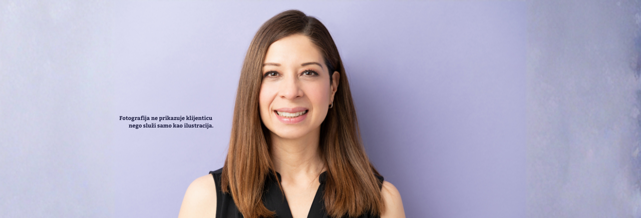 Portret nasmiješene žene s ravnom smeđom kosom, odjevene u crnu majicu, na svijetloj jednobojnoj pozadini; fotografija je ilustrativnog karaktera.